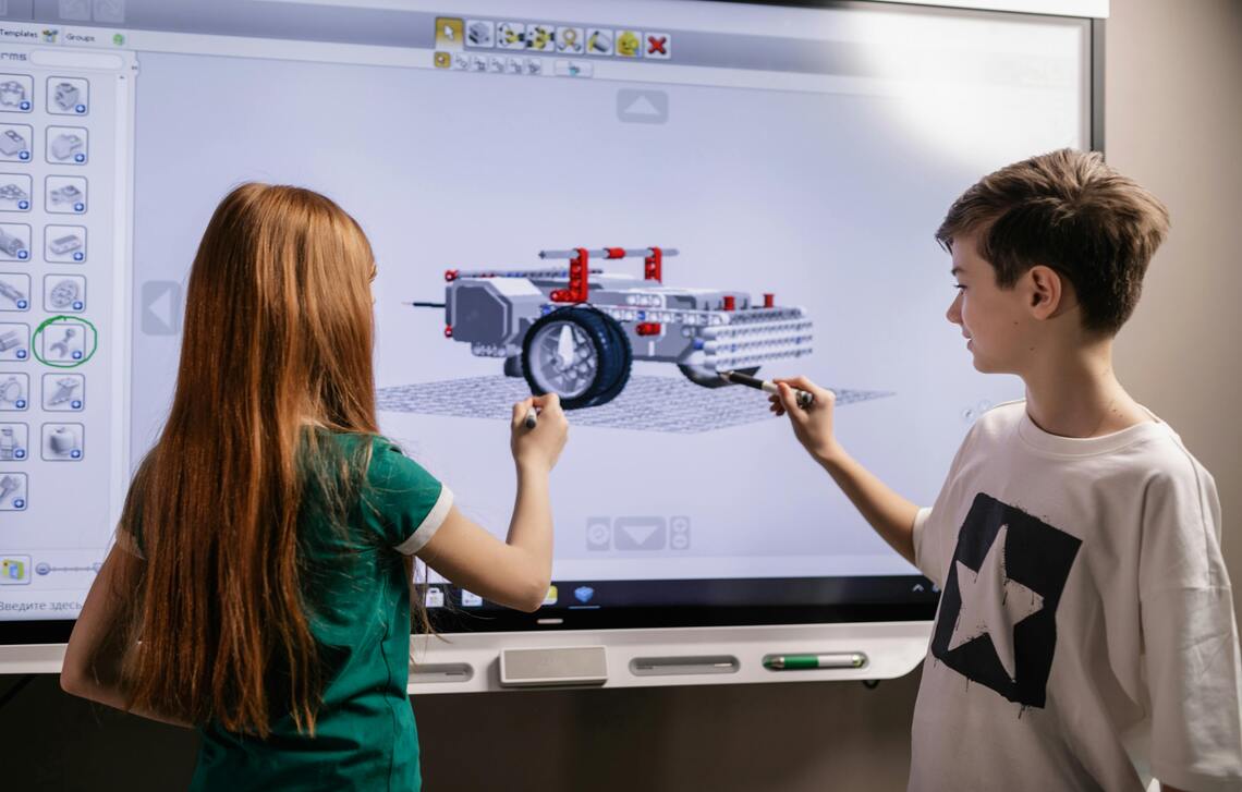 A boy and a girl standing in front of a computer screen.